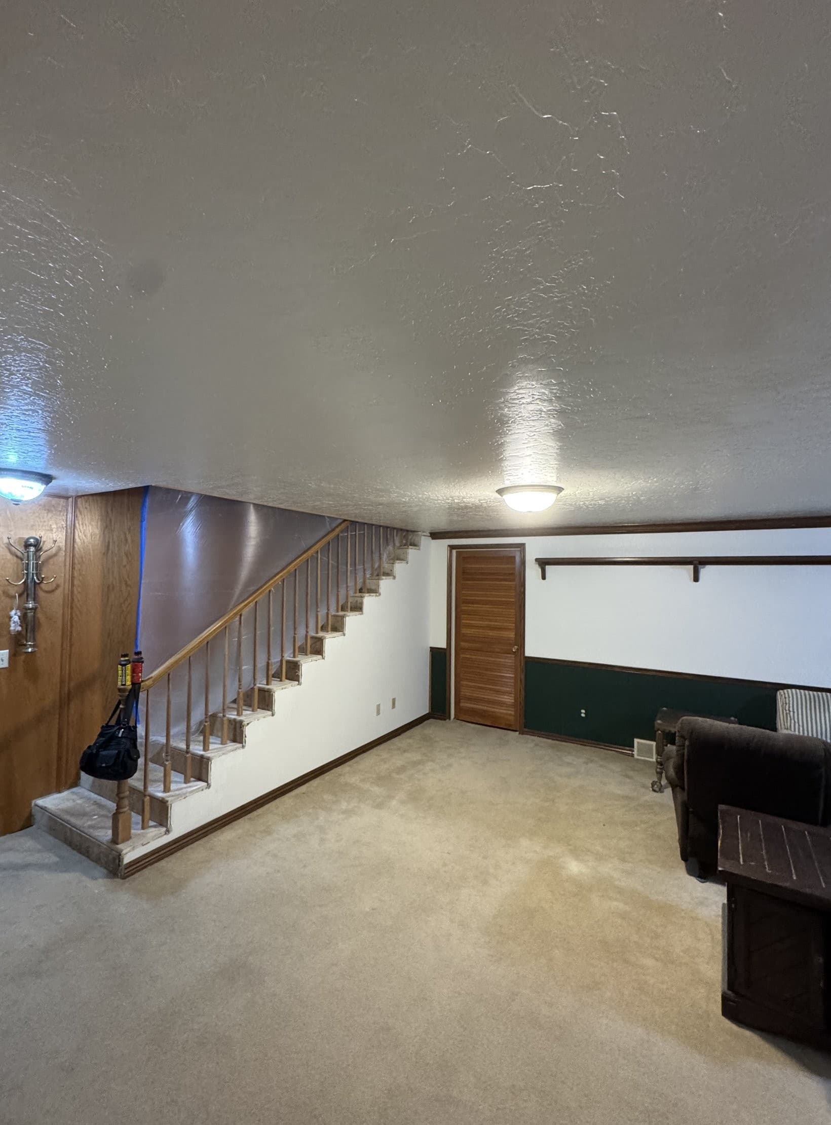 The finished basement: the new ceiling textured, painted and carrying two flush dome lights, fresh carpet laid wall to wall, and the room back in use with a sofa and side table against the far wall. The original green dado, dark chair rail, wood paneling and louvered oak door were kept.